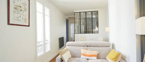 A modern living room with a sofa, a framed picture on the wall, and a large window.