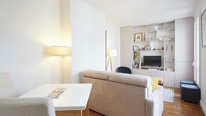 A modern living room with a sofa, a table, and a TV. There are shelves with books and decorative items. - Shared apartment in Levallois-Perret (Levallois-Perret)