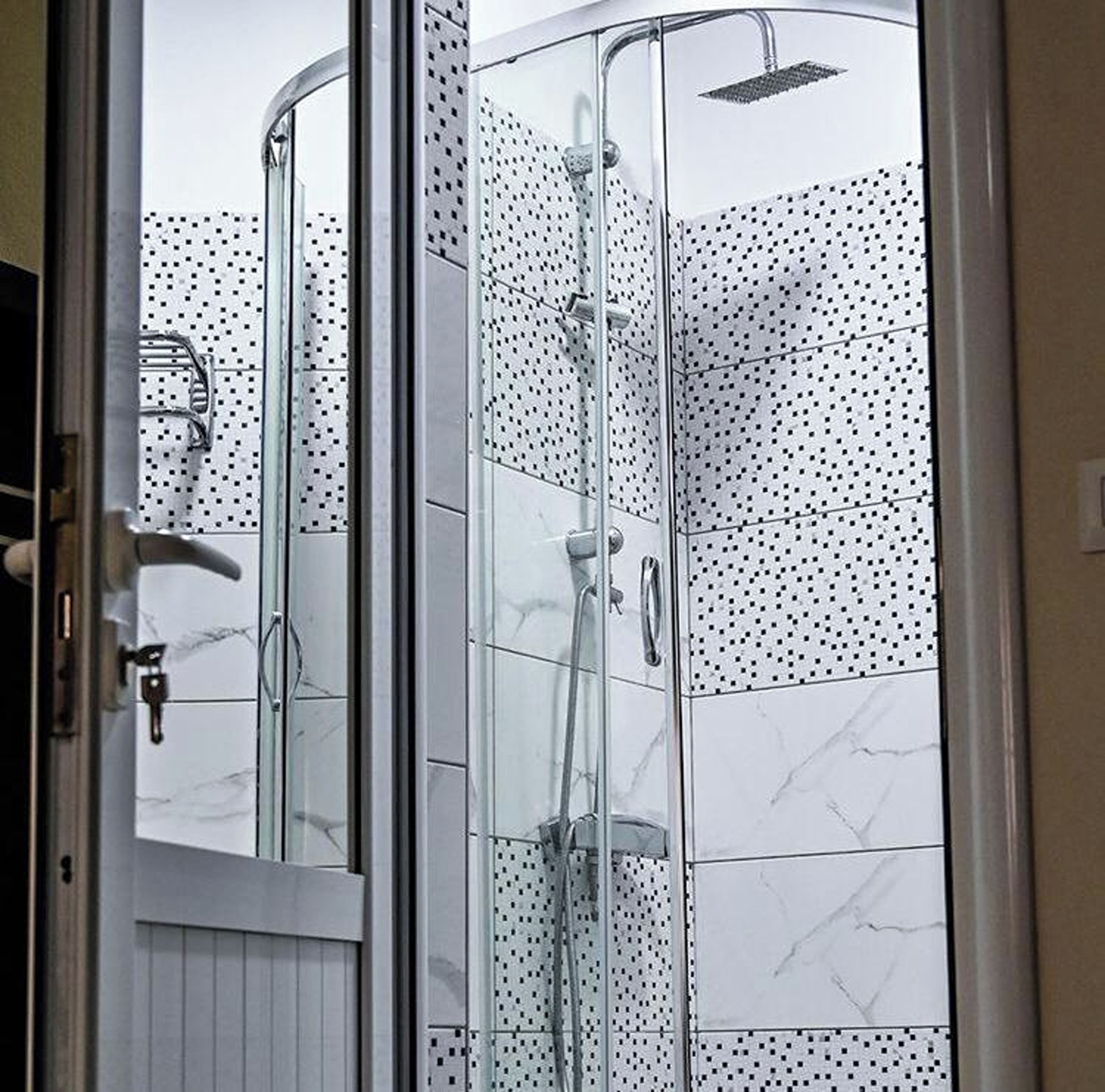 Un box de ducha con paredes de vidrio, cabezal de ducha de mano y llave en la pared.