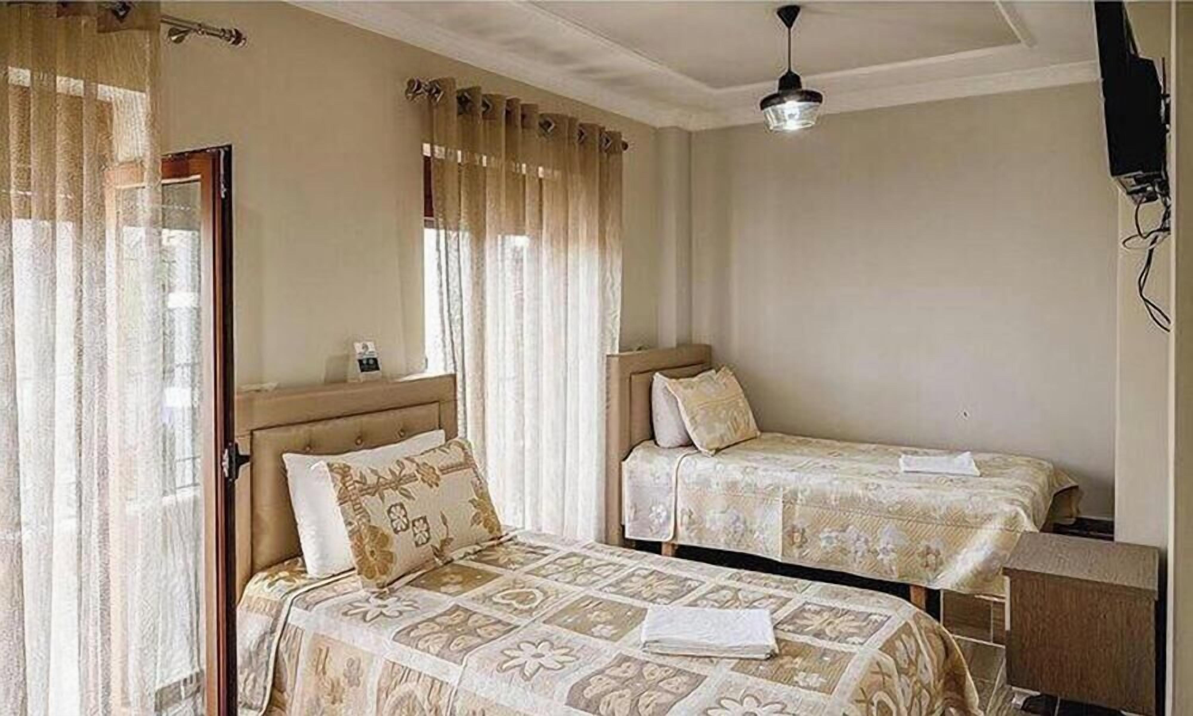 A bedroom with two beds, a wooden headboard, a bedside table, a lamp, and a ceiling light.