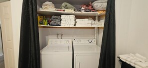 A laundry room with two stacked washers and dryers, shelves above holding folded clothes and laundry supplies. - Le Repaire Secret, a cozy and peaceful 3½-bedroom home located in the heart of the village! (Saint-Donat-de-Montcalm)