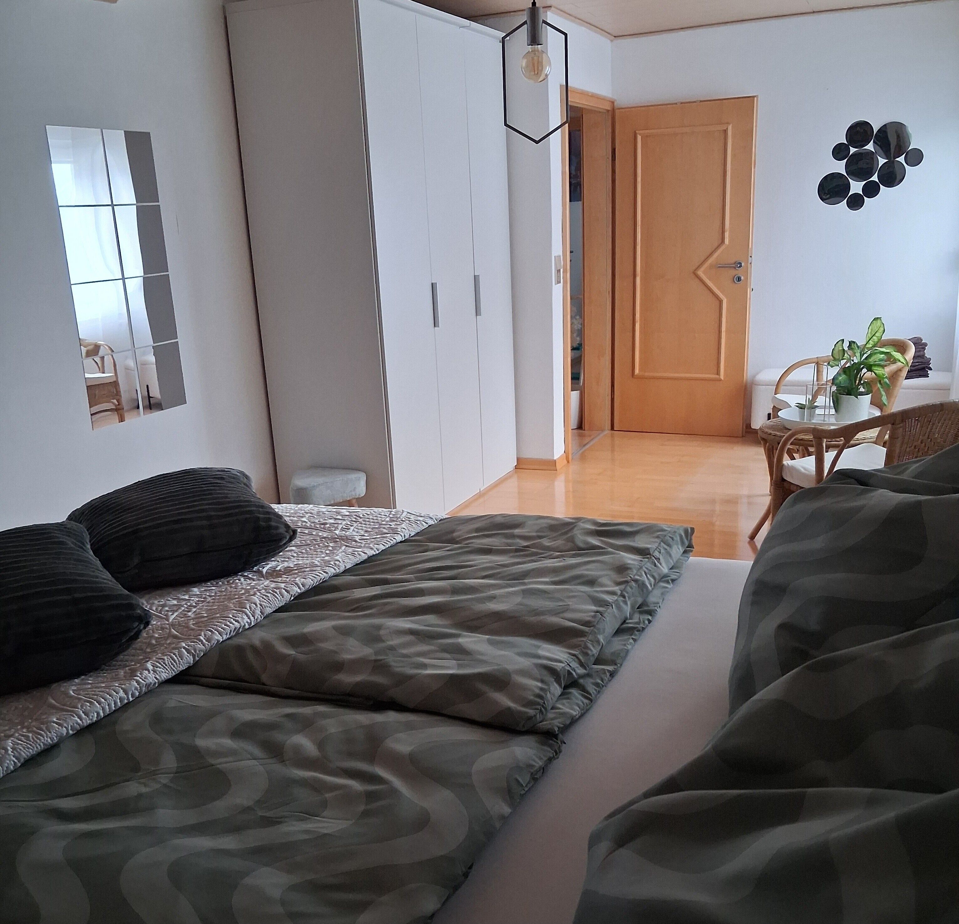 Et soveværelse med en seng, et skab, en dør, en vægdekoration og et lille bord med en plante.