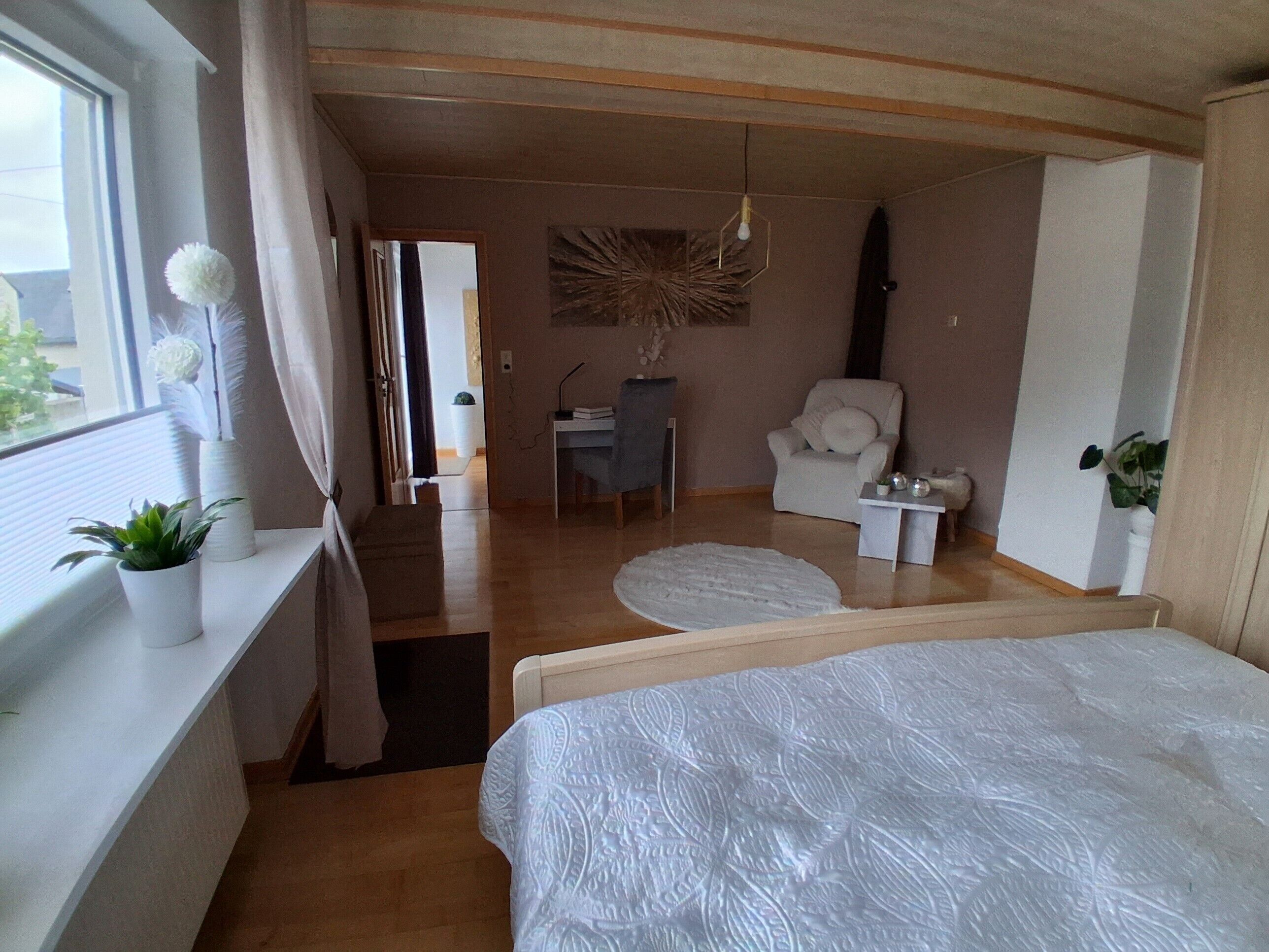 Een slaapkamer met een bed, een bureau, een stoel en een raam met gordijnen.