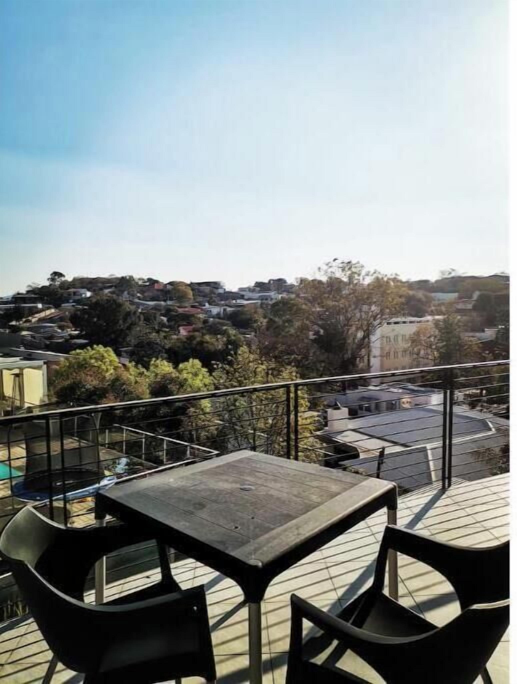 A balcony with a table and chairs, overlooking a residential area with houses and trees.