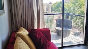 A room with a red sofa, a beige pillow, and a view of a balcony with outdoor furniture.