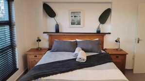A neatly made bed with a dark throw blanket, two bedside lamps, and a framed picture on the wall.