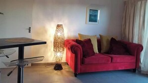 A room with a red sofa, a tall floor lamp, a framed picture on the wall, and a window with curtains.