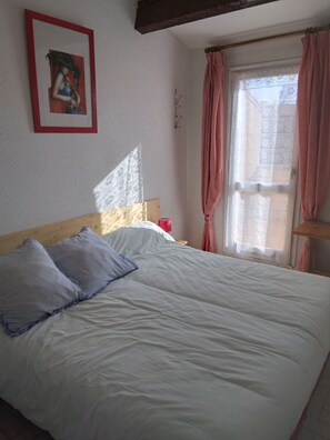 A bedroom with a bed, a painting on the wall, and a window with curtains. - Apartment for 2 to 4 people in Cap d'Agde, 200 m from La Roquille Beach (Agde)