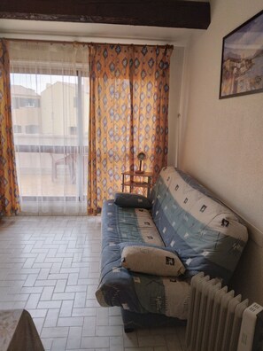 A living room with a sofa, a radiator, and a window with patterned curtains. - Apartment for 2 to 4 people in Cap d'Agde, 200 m from La Roquille Beach (Agde)