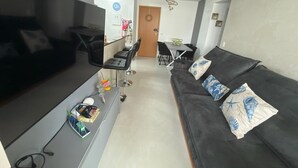 A modern living room with a sofa, a coffee table, and a dining area with a table and chairs. - NEW APARTMENT 100M FROM ASTURIA BEACH!  GUARUJA BEACH (Guarujá)