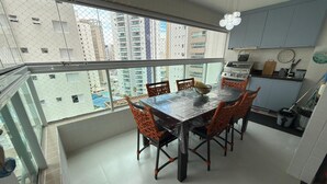 A balcony with a dining table and chairs, a kitchen area, and a view of tall buildings. - NEW APARTMENT 100M FROM ASTURIA BEACH!  GUARUJA BEACH (Guarujá)