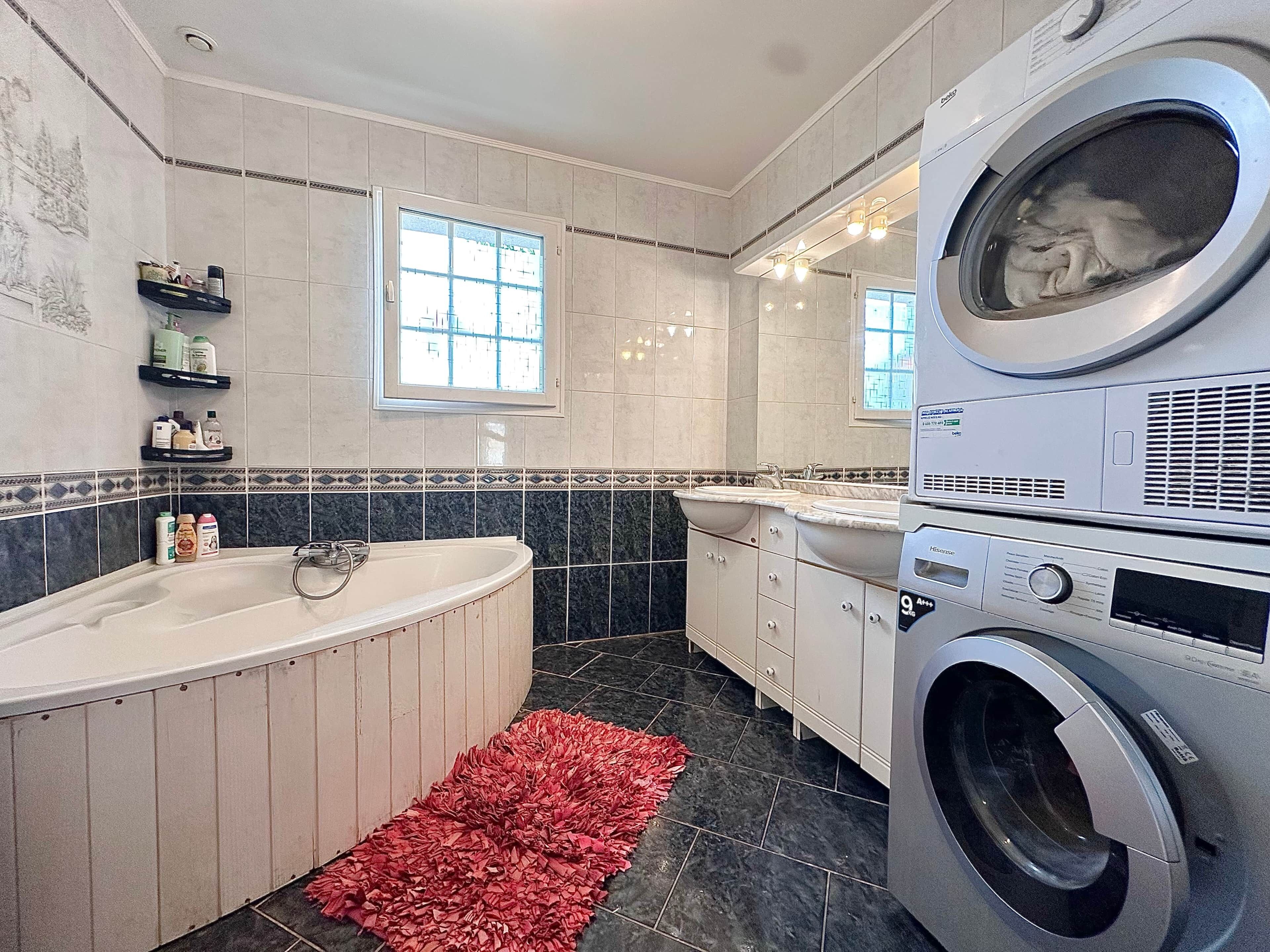 A modern bathroom with a large bathtub, a washing machine, and a vanity with a sink.