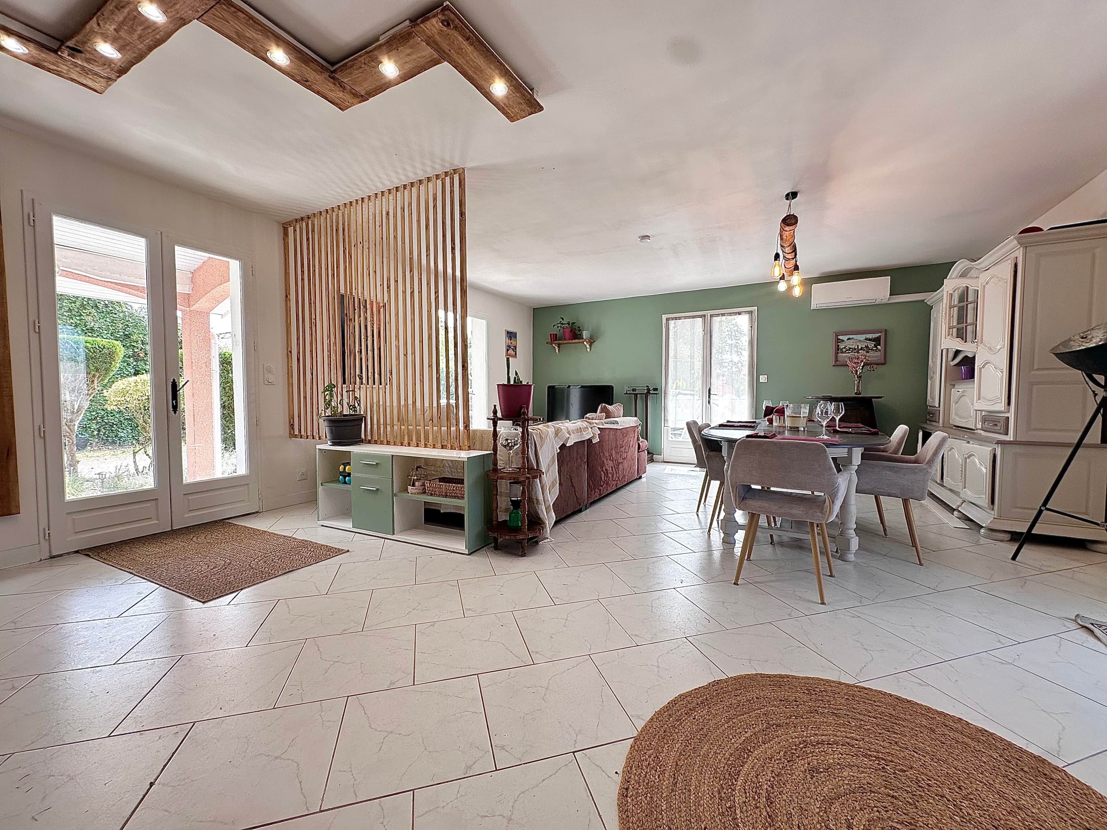 A spacious living area with a dining table, chairs, a sofa, and a kitchen area with cabinets.