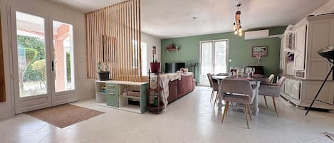 A spacious living area with a dining table, chairs, a sofa, and a kitchen area with cabinets.