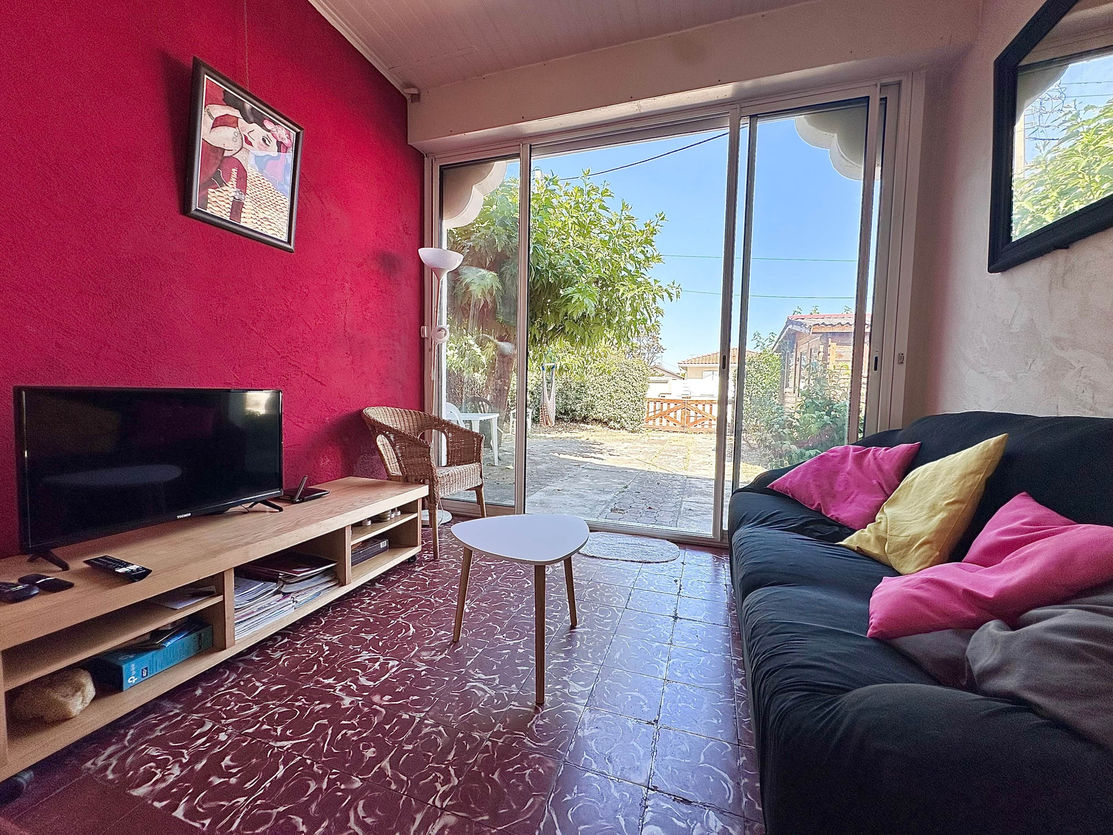 A living room with a television, a sofa with colorful cushions, a wicker chair, and a small table.