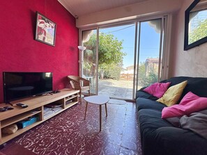 A living room with a television, a sofa with colorful cushions, a wicker chair, and a small table. - Villa Agapanthe - 3-room house near Courant (Mimizan)