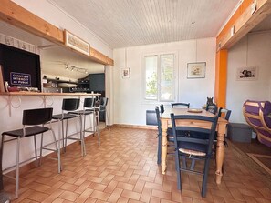 A dining area with a wooden table and chairs, a kitchen in the background, and a sign on the wall. - Villa Agapanthe - 3-room house near Courant (Mimizan)