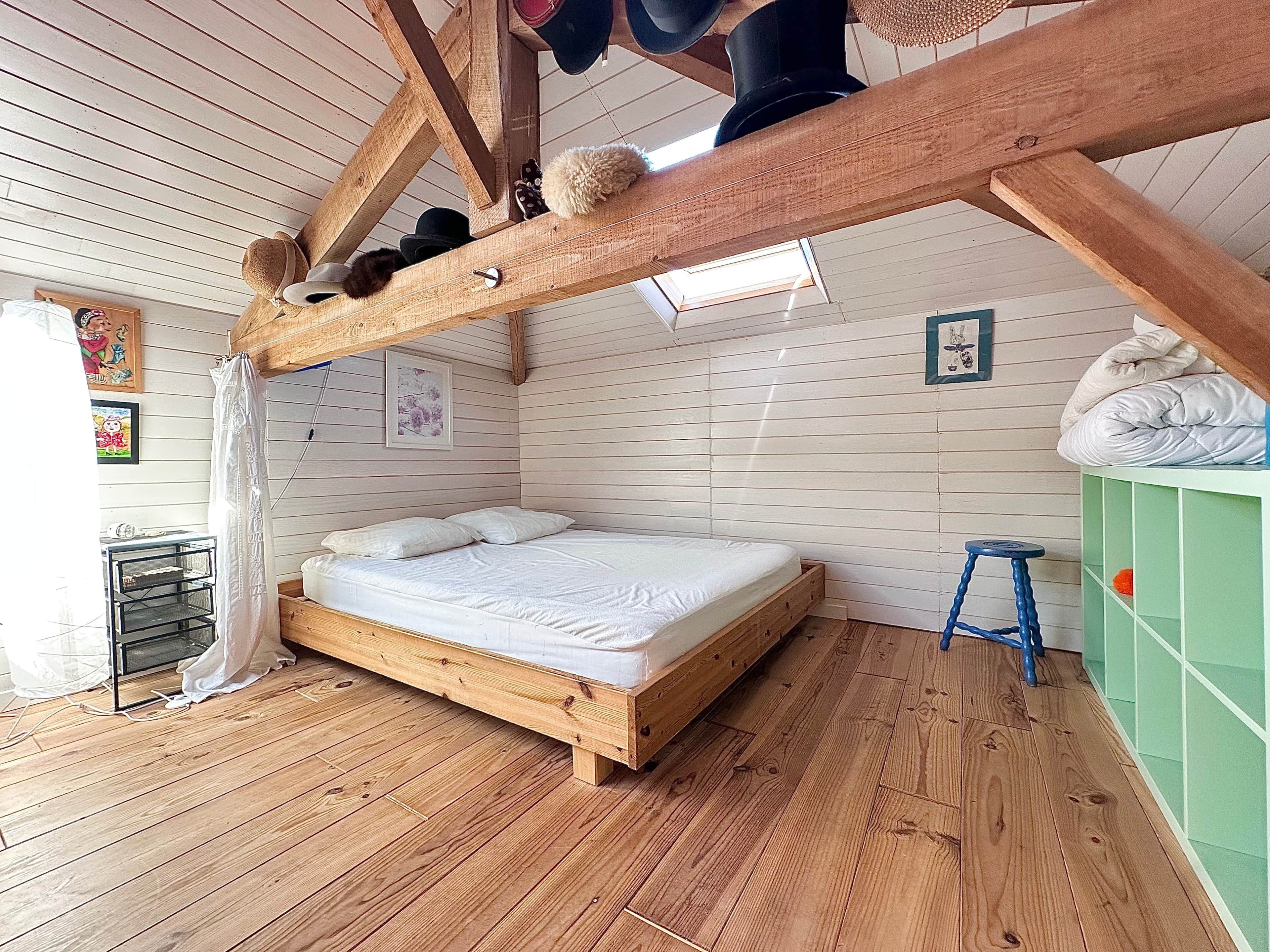 Ein Zimmer mit einem hölzernen Bett, einem Hocker und einem grünen Schrank.