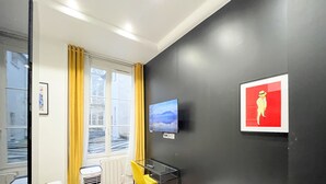 A room with a large window, a flat-screen TV, a framed picture, and a glass table. - UrbanFlat 156 - Apartment Rue Saint Denis (Paris)