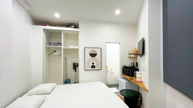 Ein Hotelzimmer mit einem Bett, einem Kleiderschrank, einem Schreibtisch mit Computer, einem Sessel und einem Fernseher.