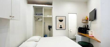 Une chambre à coucher comprenant un lit, une armoire, une salle de bain, une télévision et une étagère avec divers objets.
