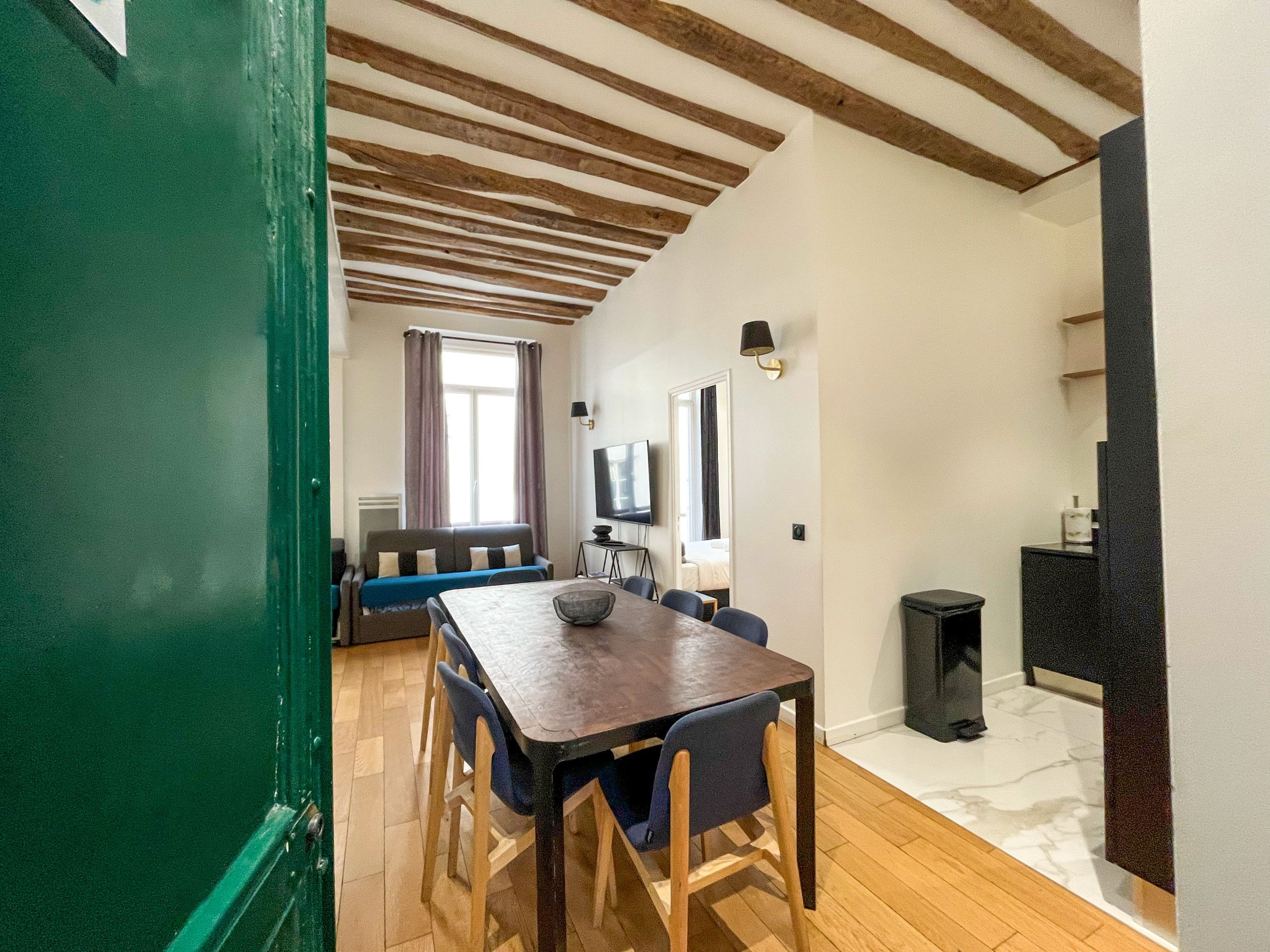 Un coin repas avec une table et des chaises en bois, un canapé et un téléviseur, le tout dans une pièce dont le plafond est orné de poutres en bois.