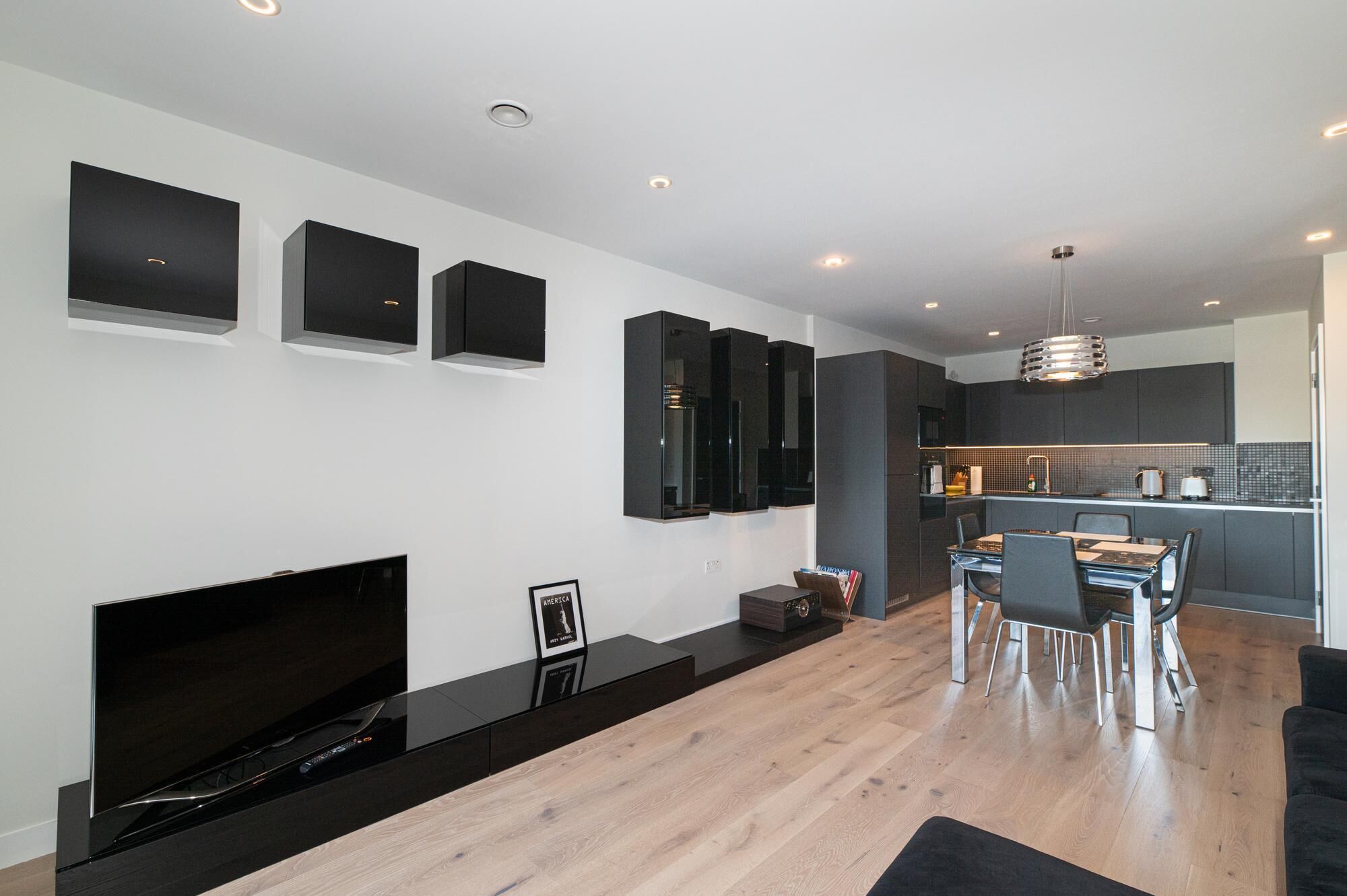 Un salon moderne doté d’un téléviseur à écran plat, d’une cheminée, d’un coin repas avec une table et des chaises, et d’une cuisine en arrière-plan.