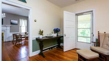 Une pièce avec un plancher en bois, un coin repas avec des chaises, une table ornée d’un vase de fleurs et une chaise avec un coussin.