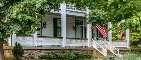A covered porch with a stone foundation, white railings, and two American flags.