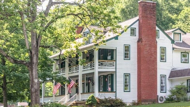 Una casa a due piani con un portico, un camino e una bandiera americana.