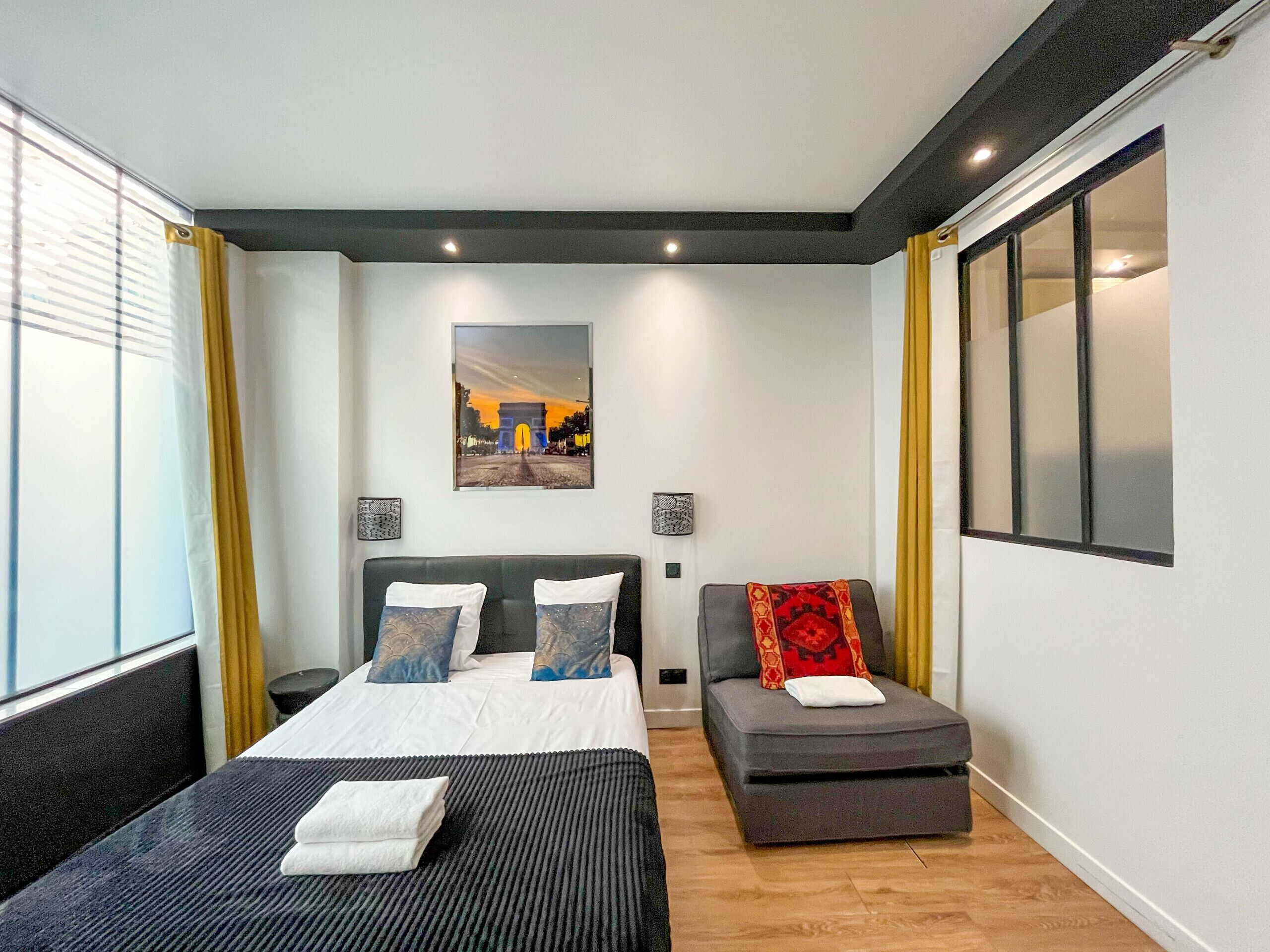 A modern hotel room with a large bed, a small sofa, and a window with curtains.