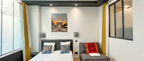 A modern hotel room with a large bed, a small sofa, and a window with curtains.
