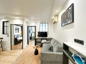 Ein modernes Wohnzimmer mit einem grauen Sofa, einem Couchtisch, einem Fernseher und einem Bild an der Wand.