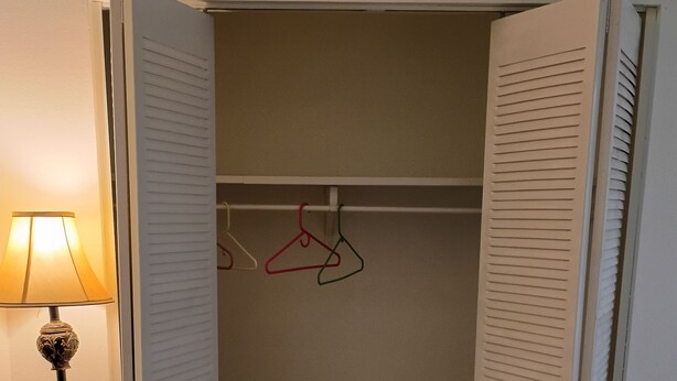 An open closet with hanging space and a floor lamp.