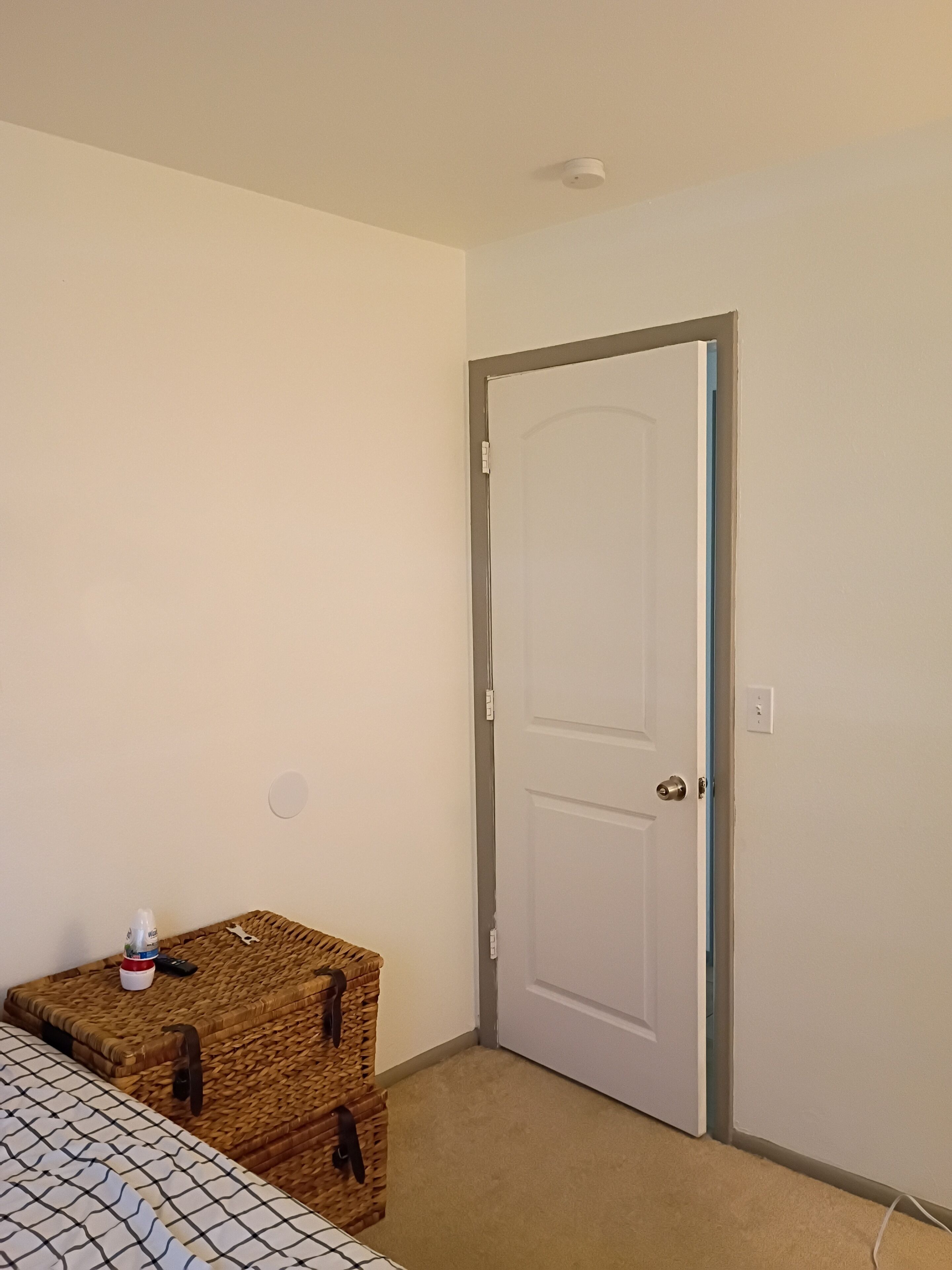 Una habitación con la puerta cerrada, una cama con una colcha estampada y dos cajas de almacenamiento de mimbre.