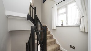 Eine Treppe mit schwarzem Geländer und beigem Teppich, die zu einer Zwischenebene mit weißer Wand und einem Fenster mit weißen Vorhängen führt.