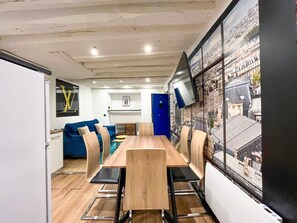 A modern dining area with a wooden table and chairs, a blue sofa, and a cityscape mural on the wall. - UrbanFlat 174 - Appartement dans le centre de Paris (Paris)