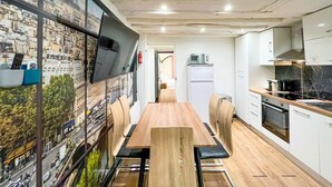 Una cocina moderna con una mesa de comedor de madera, armarios blancos y un gran mural de un paisaje urbano en la pared.