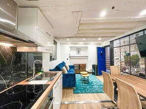 A compact kitchen with modern appliances, a dining area with a blue sofa and wooden chairs, and a large window offering a city view. - UrbanFlat 174 - Appartement dans le centre de Paris (Paris)