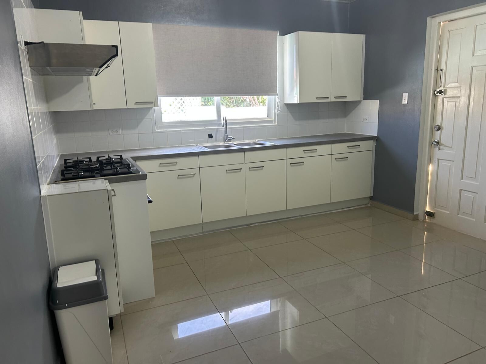 Una cocina con gabinetes blancos, una estufa a gas, un lavamanos y una ventana.