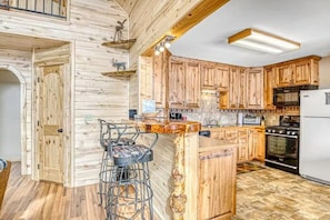 A kitchen with wooden cabinets, a bar stool, a refrigerator, and a stove. - Mountain Top Getaway 3BR Mountainview Dog Friendly (South Fork)