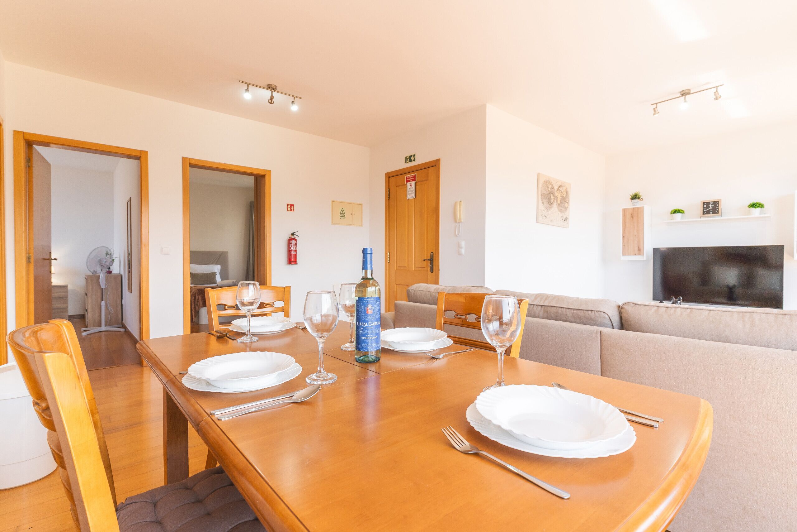 A dining area with a wooden table set for four, a sofa, and a television in the background.