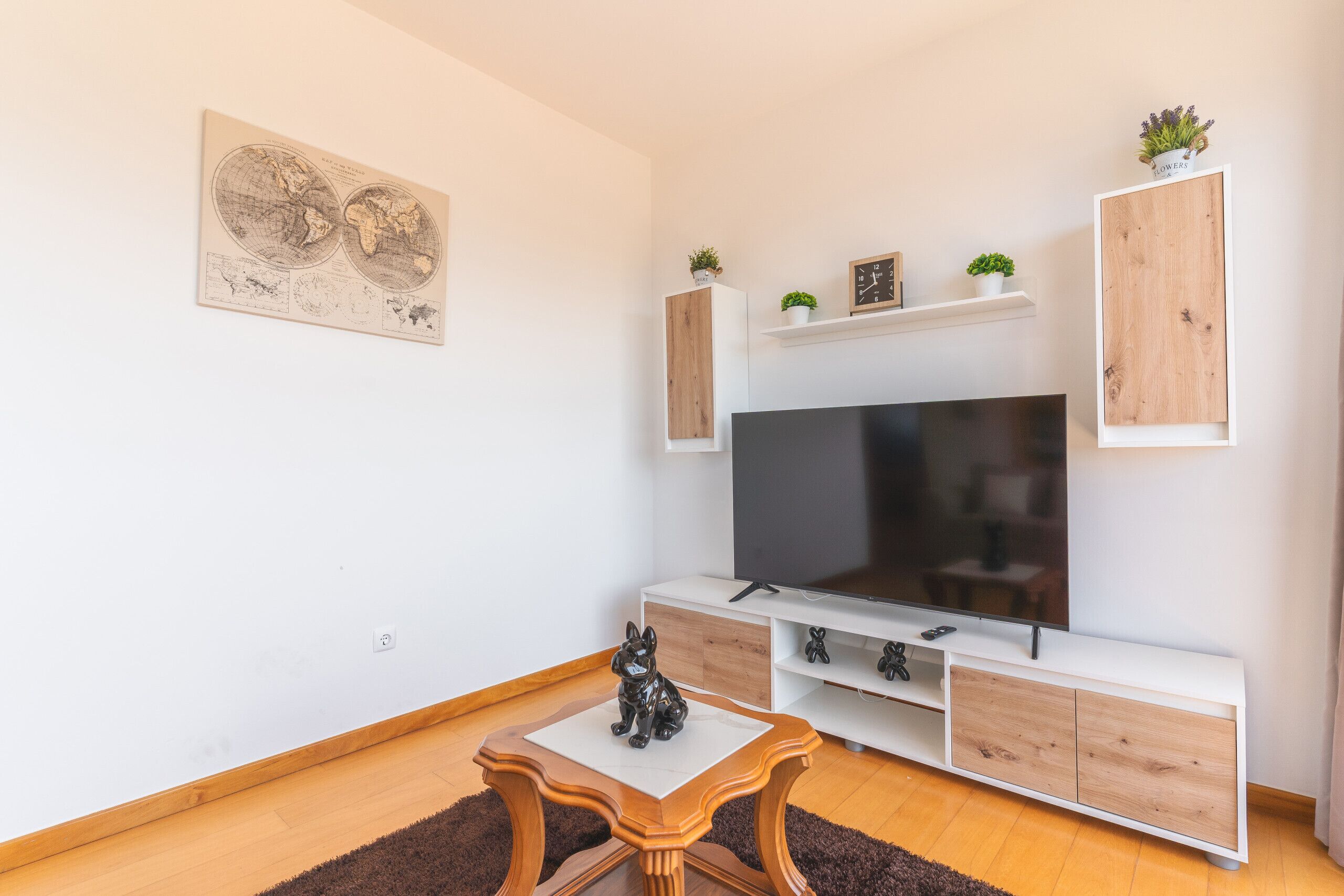 A modern living room with a flat-screen TV, wooden cabinets, a small table, and a world map artwork.