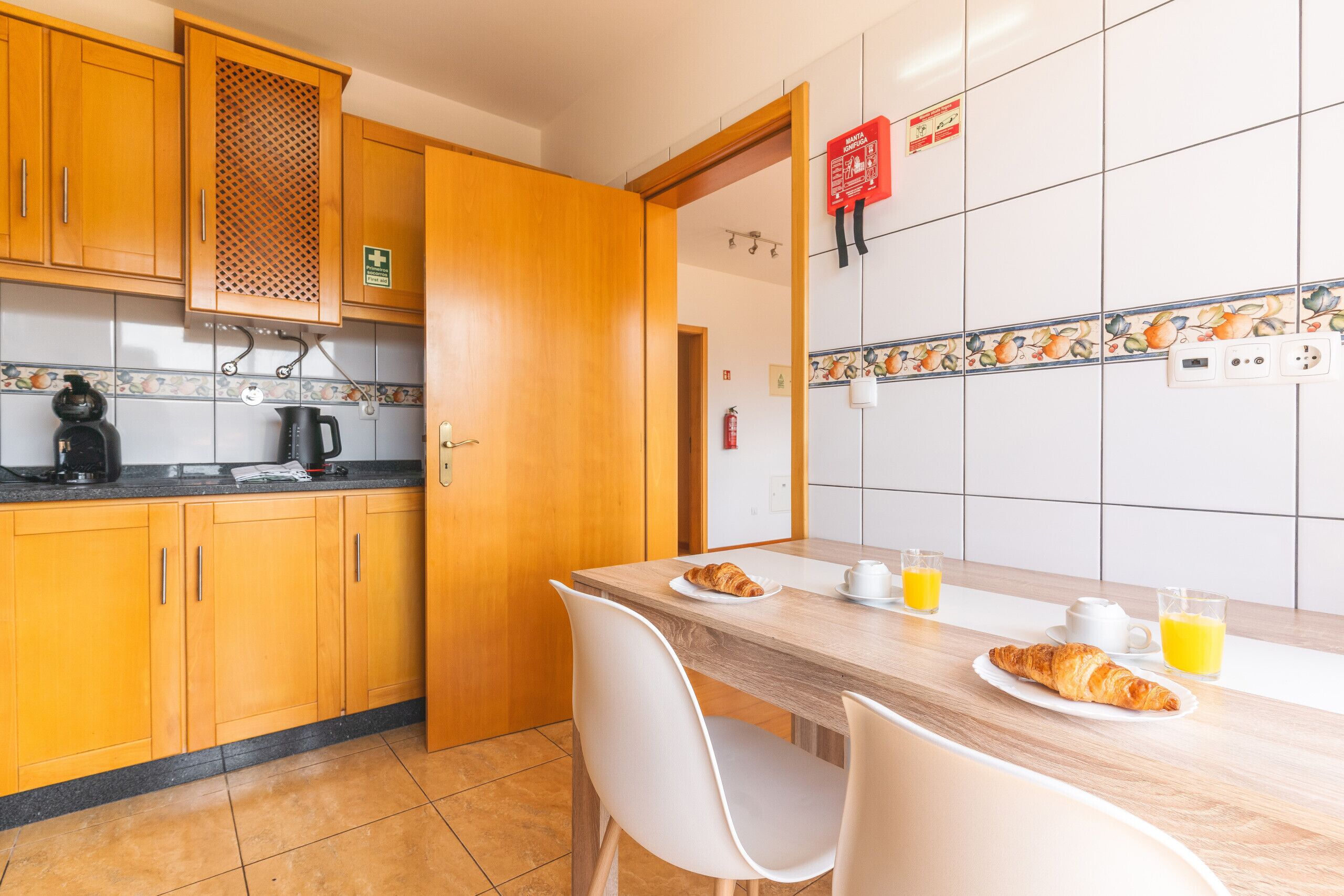 A kitchen with wooden cabinets, a coffee maker, a kettle, and a table with breakfast items.