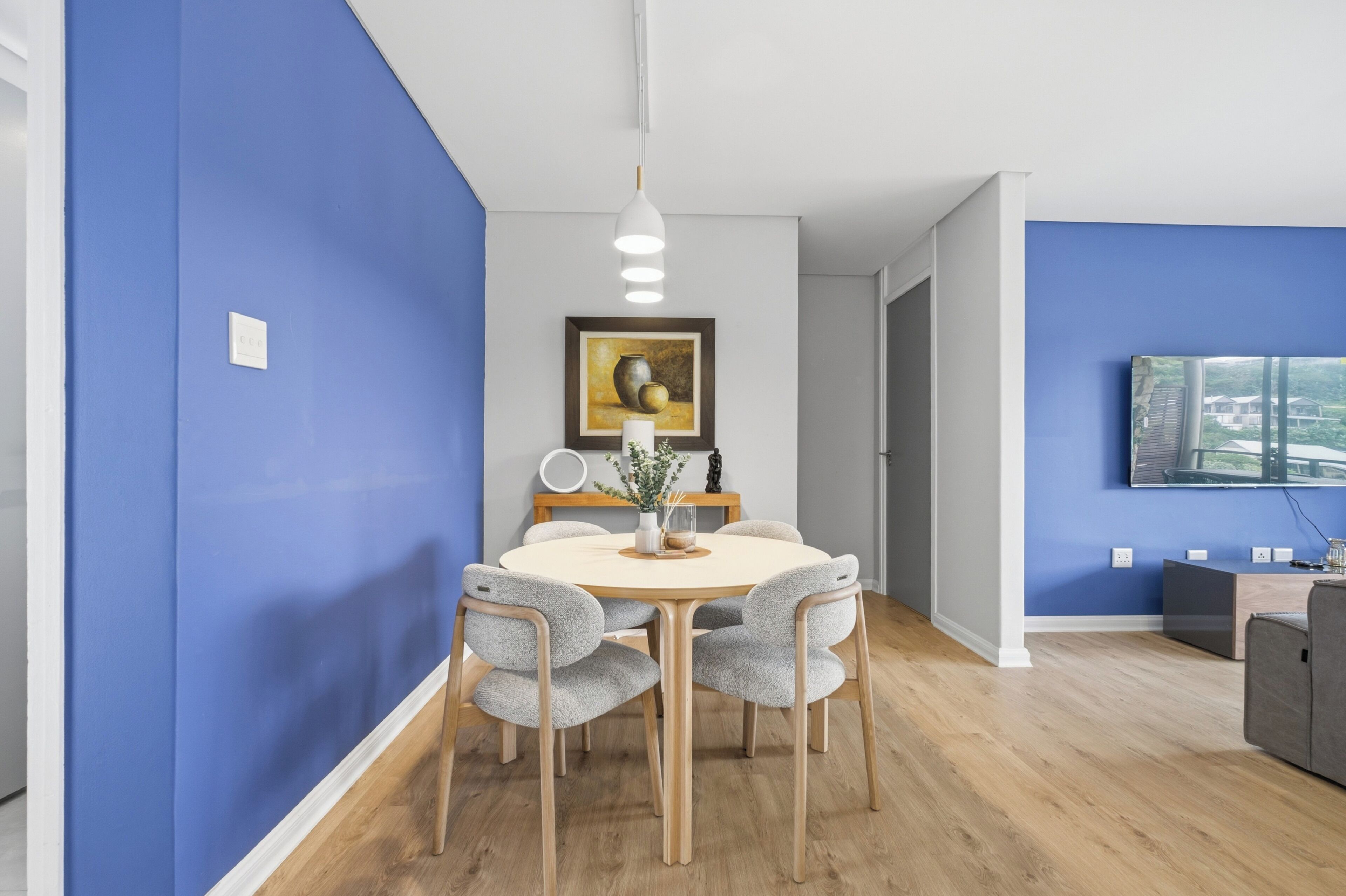 A modern dining area with a round table, four chairs, and a vase with flowers.