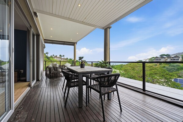 A covered outdoor area with a table and chairs, a view of the landscape, and a building in the background. - Simbithi Estate Escape | 4xBed | Air-conditioned (Dolphin Coast)