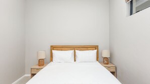 Een slaapkamer met een houten hoofdbord, twee nachtkastjes met lampen, en een groot bed met witte beddengoed.