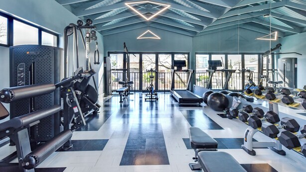 Een moderne sportschool met diverse fitnessapparaten, grote ramen en een geometrisch plafondontwerp.
