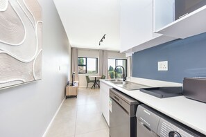 A modern kitchen with a dishwasher, a sink, and a dining area with a table and chairs. - Prime Sandton Living in Wierda Valley (Johannesburg)