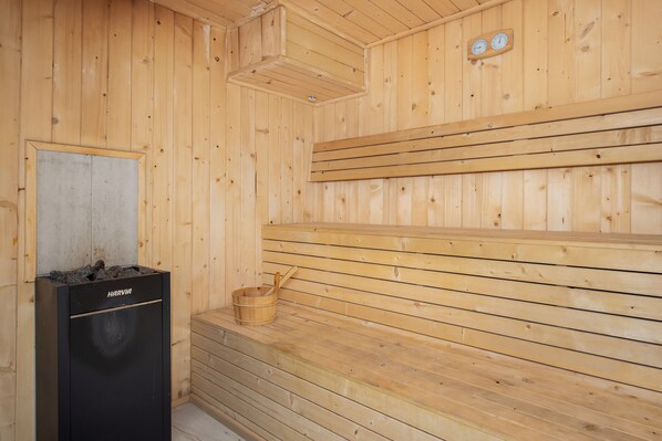 Un sauna en bois avec des bancs, un poêle de sauna de la marque Harvia et un seau en bois.